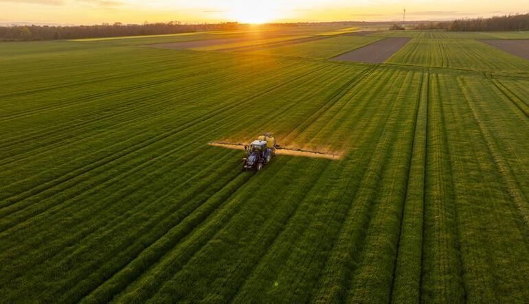 Tractor Fertilizing Verdant Agricultural Field During Golden Sunset